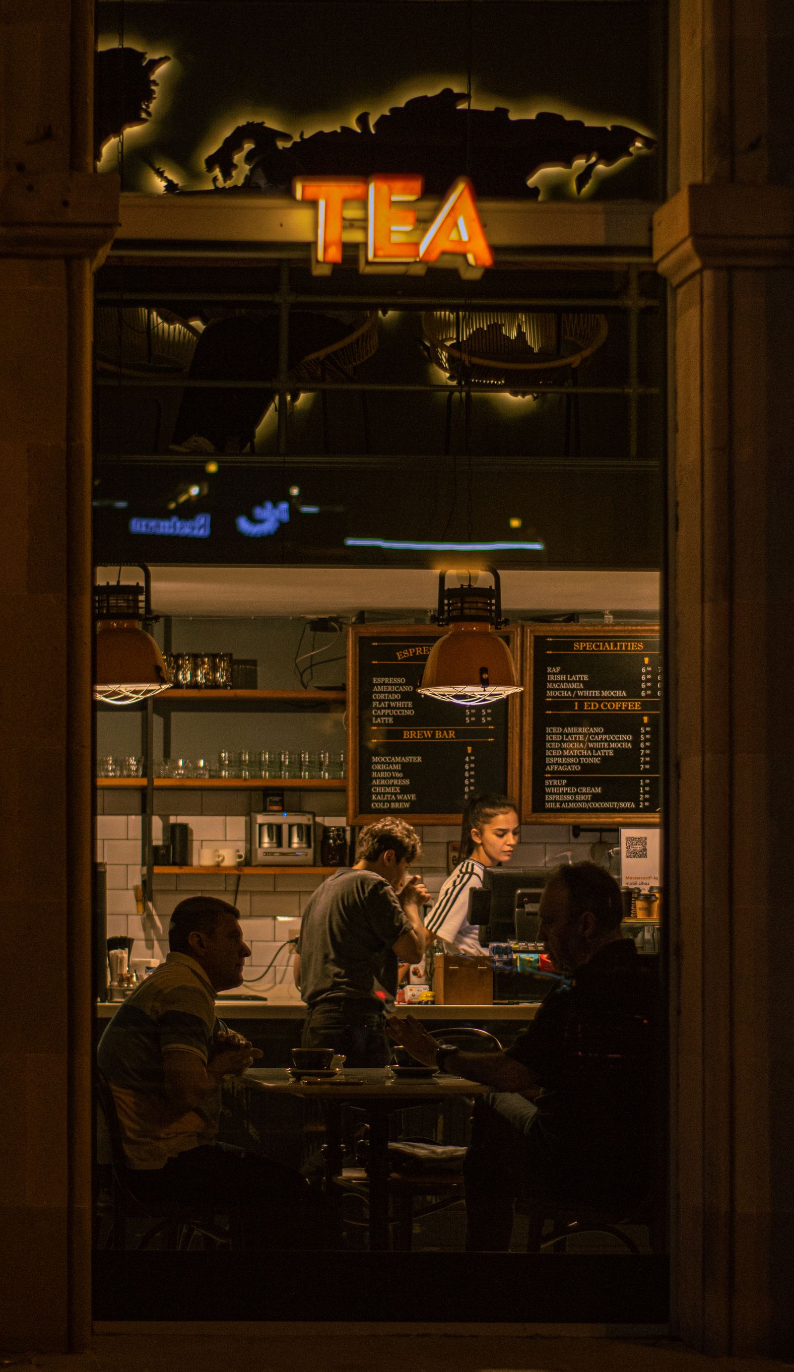 Customers inside a warmly lit cafe at night, seen from the street
