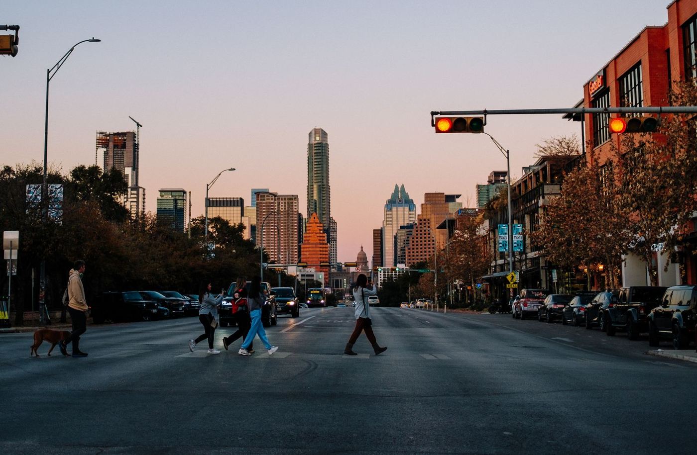 Pedestrians crossing South Congress Avenue at dusk with the downtown Austin skyline and Texas Capitol